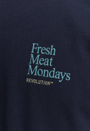 Marineblaue Baumwollbluse mit gerippter Textur, auf der in Hellblau gedruckt steht: "Fresh Meat Mondays" und in Gelb "REVOLUTION™".