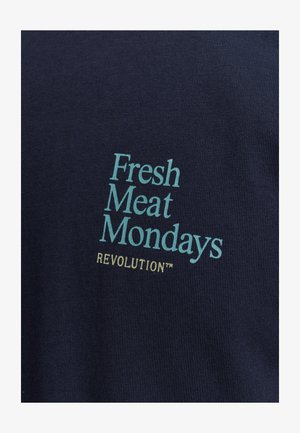 Navy blue cotton shirt with ribbed texture featuring printed text: "Fresh Meat Mondays" in light blue and "REVOLUTION™" in yellow.