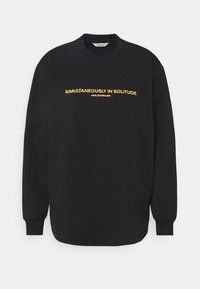 Czarna bluza z bawełny, z okrągłym dekoltem i długimi rękawami. Z przodu widnieje żółty napis "JEDNOCZEŚNIE W OSOBCIE".