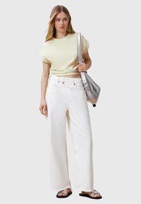 Korte, lichtgele katoenen t-shirt gecombineerd met witte, wijde denim jeans met rafelige zomen. Accessoires zijn een metallic zilveren tas en sandalen.