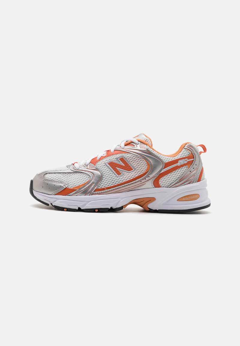Baskets de sport argentées et oranges avec une tige en maille, un col rembourré et une semelle en caoutchouc. Elle présente un logo "N" bien visible et des lignes de design élancées.