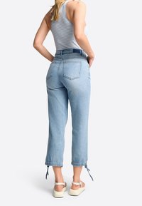 Jeans de tiro alto azul claro con un corte holgado, que cuentan con bolsillos traseros y dobladillos ajustables con cordón. El conjunto se complementa con sandalias blancas.