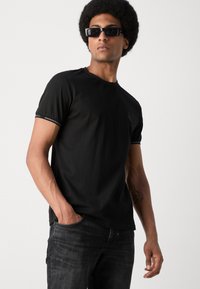 Zwart T-shirt met korte mouwen van katoen, met een ronde halslijn en geborduurd logo op de borst, gecombineerd met donkergrijze spijkerbroek.