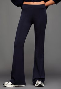 Granatowe dzwony wykonane z miękkiego, elastycznego materiału o gładkiej fakturze, z wysokim stanem i pionowymi szwami nadającymi elegancki wygląd.