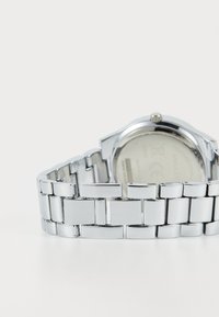 Reloj de pulsera de metal plateado con una pulsera de eslabones pulidos, caja redonda y un fondo visible. Acabado suave y brillante con eslabones rectangulares.