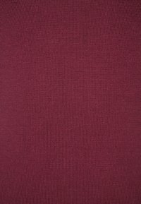 Tessuto lavorato a maglia di un profondo bordeaux con una sottile texture a coste, creando un motivo uniforme sulla superficie.