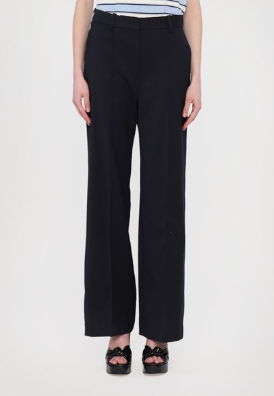 Pantaloni evazați dintr-un material solid bleumarin, cu talie înaltă și pliuri frontale, asortați cu pantofi cu platformă negri. Textură netedă și croială ajustată.