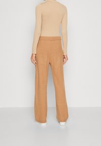 Beige langærmet top parret med lysebrune brede bukser, lavet af blødt stof, med en subtil tekstur og elastisk talje.