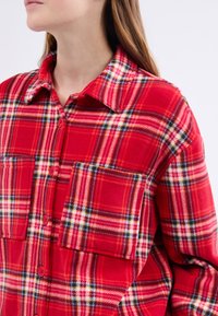 Czerwona, w kratę flanelowa koszula z dużymi deseńami, zapinana na guziki, z kołnierzykiem i pojedynczą kieszenią na piersi o miękkiej teksturze.