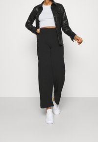 Czarne spodnie z szerokimi nogawkami o gładkiej teksturze, w połączeniu z białym krótkim topem i czarną skórzaną koszulą zapinaną na guziki, dopełnione białymi sneakersami.