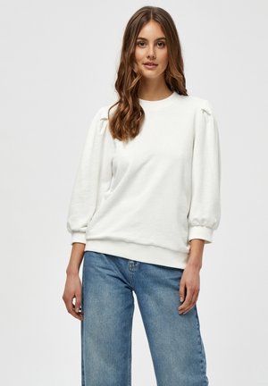 White sweatshirt with puffed sleeves, ribbed cuffs, and hem. Soft texture, paired with light blue denim jeans, creating a casual look.