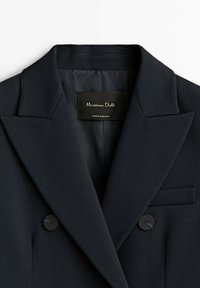 Veste noire croisée à revers crantés et deux boutons visibles, avec une étiquette noire « Massimo Dutti » à l’intérieur du col.