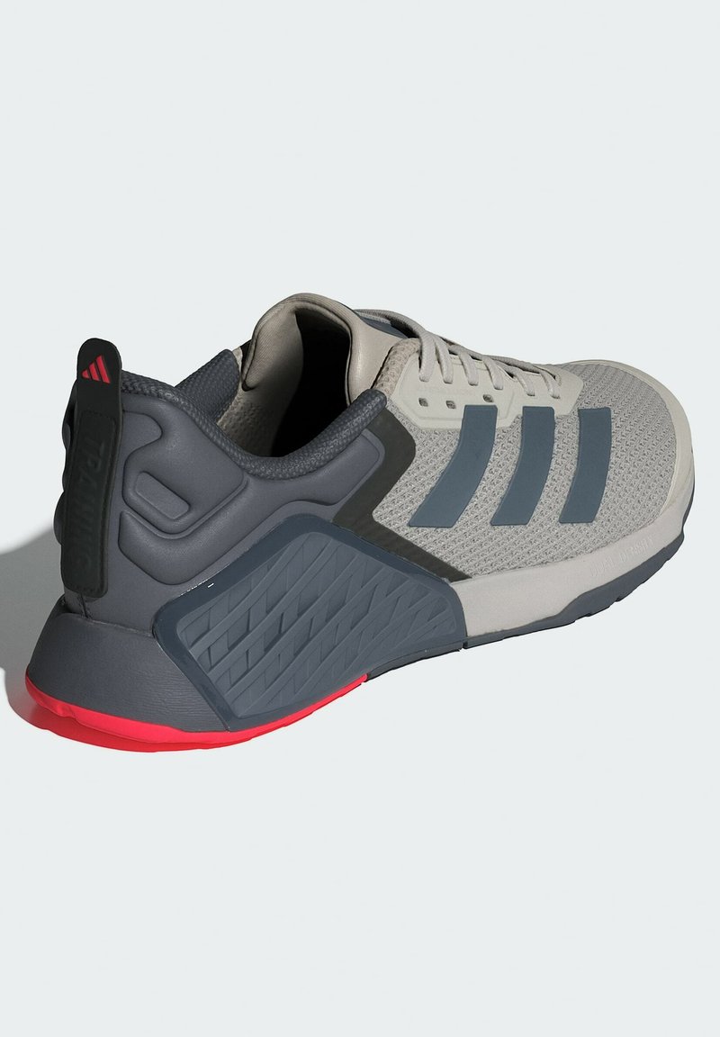 Szare buty sportowe z oddychającą siateczką, trzema ciemnoszarymi paskami, gumową podeszwą oraz czerwonymi akcentami na pięcie. Posiadają teksturowaną osłonę pięty.