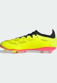 Chaussure de football jaune vif avec une tige texturée, des lacets noirs et une semelle rose. Elle est dotée de la technologie hybride touch et de crampons moulés.
