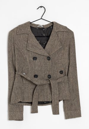 Hnědý tvídový dvouřadý blazer s černými knoflíky a látkovým páskem zavěšený na černém ramínku na bílém pozadí.