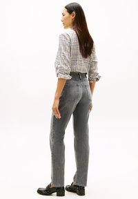 Γκρι τζιν με ψηλή μέση και ίσια γραμμή, πίσω τσέπες και υφασμένη μπλούζα με καρό σχέδιο και γυρισμένα μανίκια. Μαύρα παπούτσια με χοντρό τακούνι ολοκληρώνουν το σύνολο.