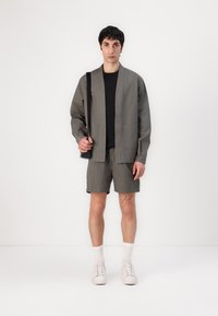 Grå bomulljakke med åpen front og lommer, sammen med matchende shorts. Hvite sneakers og ribbede sokker fullfører antrekket.