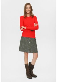 Crvena majica dugih rukava u kombinaciji s suknjom od houndstooth uzorka u sivoj boji s prednjim gumbima. Smeđe čizme do koljena upotpunjuju outfit.