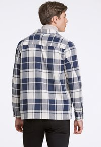 Camicia in flanella da uomo in plaid navy e crema, con colletto button-down, maniche lunghe e finitura testurizzata. La vista posteriore mette in evidenza i dettagli del design.
