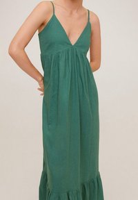 Zelené lněné šaty s tenkými ramínky, hlubokým výstřihem do V, nařaseným živůtkem a volánovým lemem, s volným střihem a měkkou texturou.