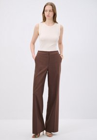 Pantaloni marroni a gamba larga con una vestibilità sartoriale, tasche laterali e una texture liscia. Abbinati a un top senza maniche di un leggero beige.