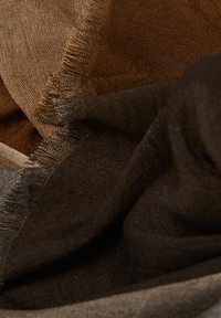 Tissu tissé marron et doré au toucher doux, avec des drapés superposés et des bords frangés, créant un effet de brillance subtil.