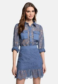 Blouse en dentelle bleue avec deux poches poitrine et des détails de boutons, associée à une jupe en dentelle assortie avec un motif floral et un ourlet à volants.