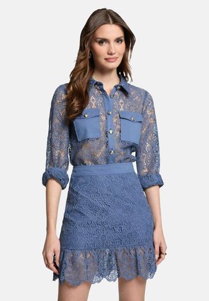 Blouse en dentelle bleue avec deux poches poitrine et des détails de boutons, associée à une jupe en dentelle assortie avec un motif floral et un ourlet à volants.
