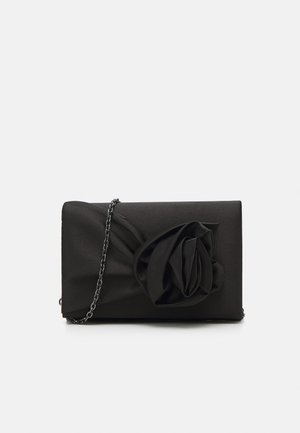 Zwarte rechthoekige clutch met een grote stoffen roos en een dunne kettingriem op een witte achtergrond.