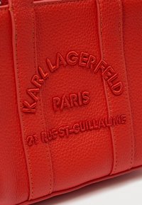 Piros, textúrált bőrtáska, az elején varrott "Karl Lagerfeld Paris" márkanevével és a "21 Rue St-Guillaume" címmel.