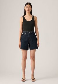 Σορτς από τζιν με ψηλή μέση σε σκούρο μπλε, με ακατέργαστο τελείωμα, εμπρός τσέπες, κλείσιμο με κουμπί και εφαρμοστή σχεδίαση. Συνδυάζεται με μαύρο αμάνικο τοπ.