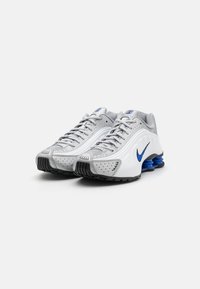 Nike tenisice s gornjim dijelom od sivog mrežastog i sintetičkog materijala, bijelim detaljima, plavim logom i crnom gumenu potplatom s vidljivim elementima zračne amortizacije.