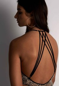 Design noir à dos strappy avec plusieurs fines bretelles. Le vêtement présente un imprimé zèbre beige et noir sur une texture de tissu lisse.