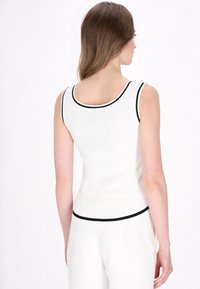 Weißes, geripptes Tanktop mit schwarzem Saum am Hals und am Saum. Enganliegendes Design mit rundem Rücken, aus einem glatten, dehnbaren Stoff gefertigt.