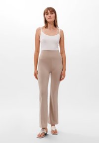 Jasnobeżowe, rozszerzające się spodnie z wysokim stanem, wykonane z miękkiego, elastycznego materiału. W zestawie z białym topem na ramiączkach i płaskimi sandałami.