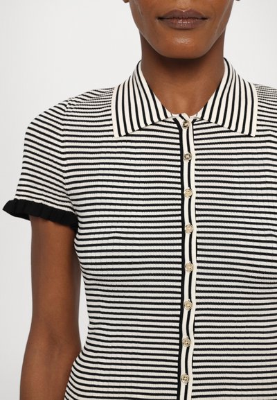 Blusa de manga corta a rayas blancas y negras con cuello tipo camisa, textura acanalada y botones decorativos a lo largo de la tapeta frontal.
