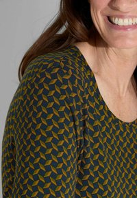 Korte mouw shirt van donkerblauwe stof met een geometrisch patroon van gele en olijfachtige vormen; zachte textuur en ronde halslijn.