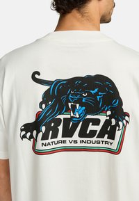 Witte katoenen T-shirt met een zwart pantergrafiek, blauwe accenten en vetgedrukte tekst "RVCA" en "NATURE VS INDUSTRY" eronder.