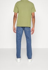 T-shirt en coton olive, coupe décontractée, manches courtes et col rond, assorti à un jean en denim bleu et des baskets blanches.