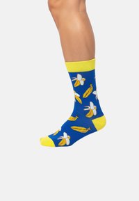 Blaue Socken mit gelben Akzenten, die ein Bananenmuster und weiße Blumenmuster aufweisen. Hergestellt aus weichem Material, knielange Passform.