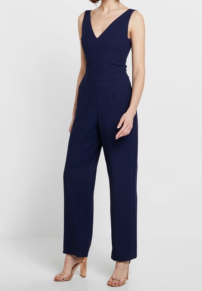 Mörkblå byxdress med djup V-ringning, ärmlös design, skräddarsydd passform och vida ben. Har diskreta veck och en mjuk textur.
