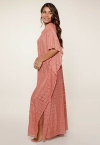 Vestido maxi de encaje ligero de color rosa con mangas cortas, que presenta un diseño de tejido abierto y una abertura lateral para facilitar el movimiento.