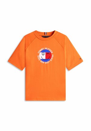T-shirt orange vif à manches courtes arborant un logo circulaire avec un signe de paix, un smiley qui fait un clin d'œil, et le texte « Tommy Hilfiger Peace Love and Soul ».