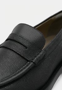 Mocassin en cuir noir avec une finition texturée, doté d'une large bande et d'accents cousus. Bout arrondi et doublure intérieure lisse.