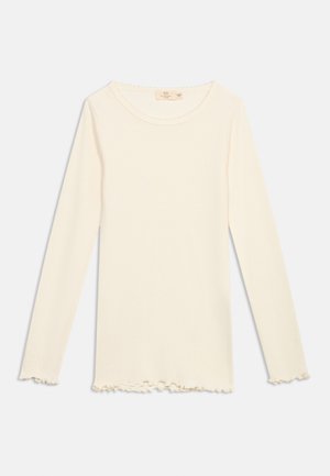 Langermet kremfarget ribbestrikket skjorte med rund hals og krusede kanter på ermer og nederst.