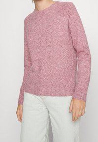 Rosa gestrickter Pullover mit rundem Ausschnitt, gerippten Bündchen und Saum, weiche Textur, figurbetonter Stil, lange Ärmel, gefertigt aus warmem, flauschigem Material.