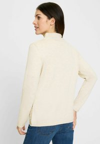 Helles beiges Sweatshirt mit hohem Kragen und langen Ärmeln. Verfügt über gerippte seitliche Akzente und eine strukturierte Strickoberfläche. Lässiger Schnitt.