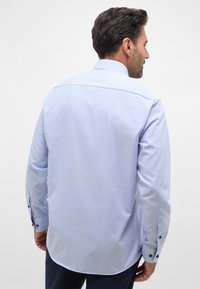 Camicia a maniche lunghe a quadri blu chiaro con polsini a bottoni, cucitura posteriore dritta e colletto classico. Tessuto morbido.