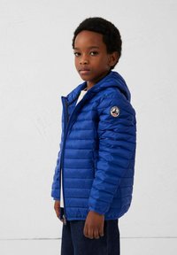 Blauwe pufferjas met een doorgestikt ontwerp, rits aan de voorkant en een capuchon. Voorzien van een ronde logopatch op de linkermouw. Lichtgewicht materiaal.