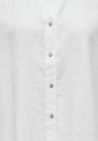 Tissu en lin blanc avec une rangée verticale de cinq boutons nacrés sur la fermeture avant d'une chemise ou d'un chemisier.